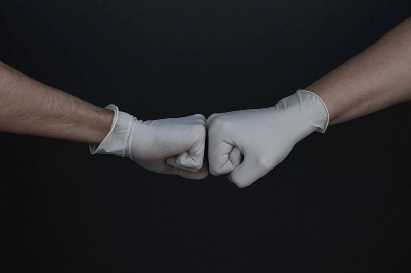 Two people fist-bumping while wearing protective gloves