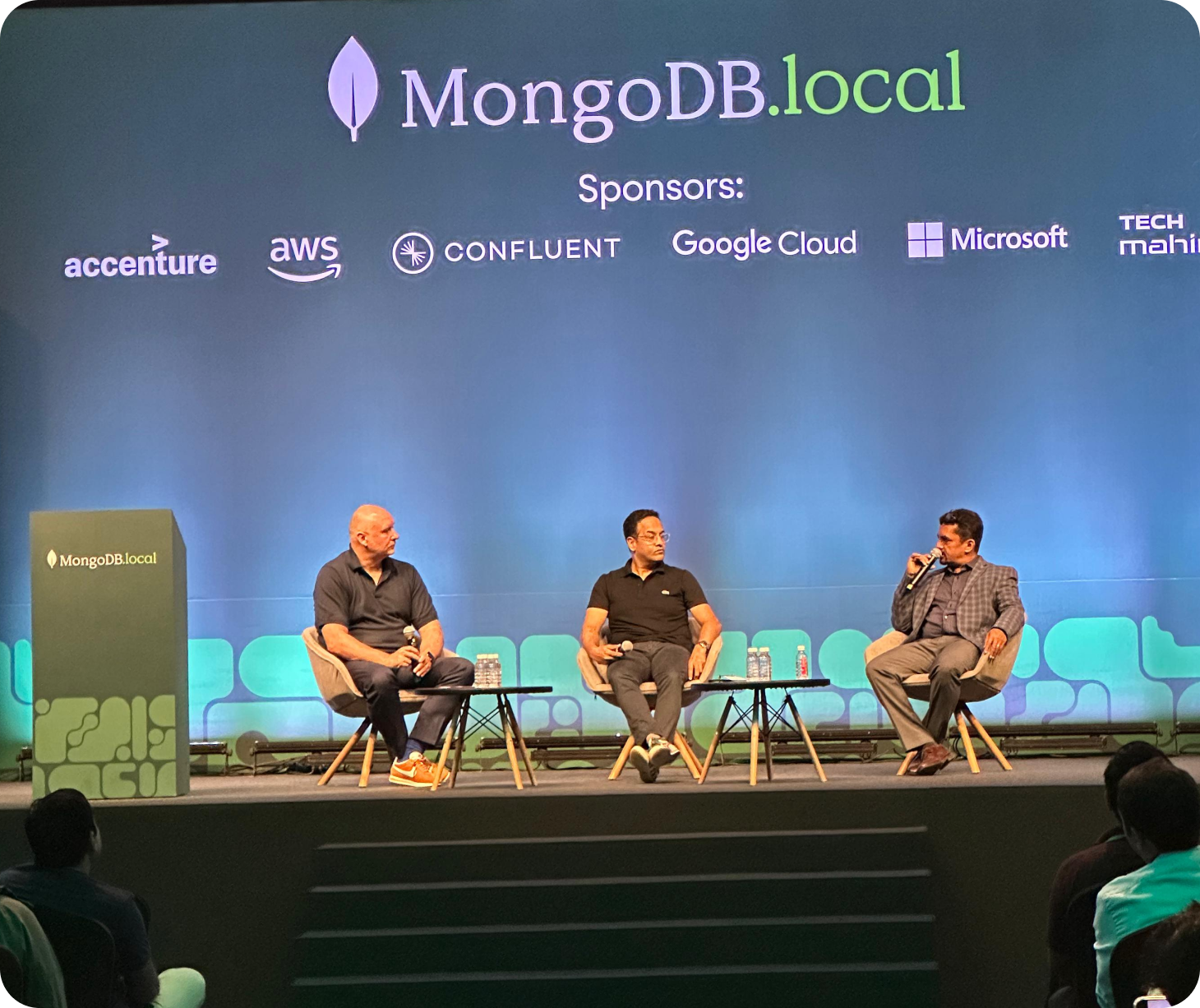 Three panellists seated on stage under the MongoDB.local Bengaluru screen, with the sponsor line visible above them.
