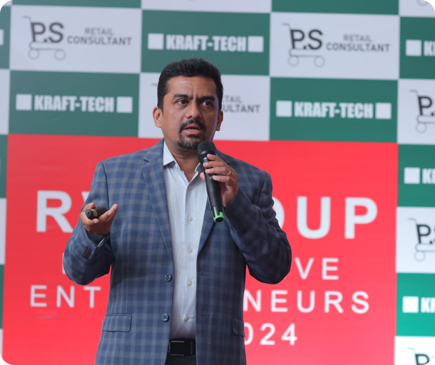 Raj Gopal speaking into a microphone on stage at the RV Group Progressive Entrepreneurs Meet 2024, in front of the event backdrop.